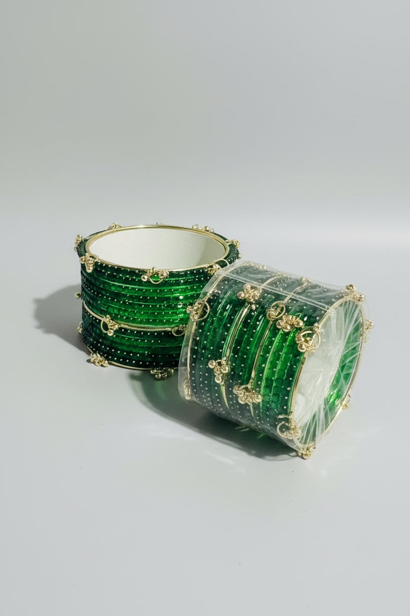 A stack of green beaded bangles with gold-tone metal borders and decorative charms, displayed on a stand with a matching packaged set below.