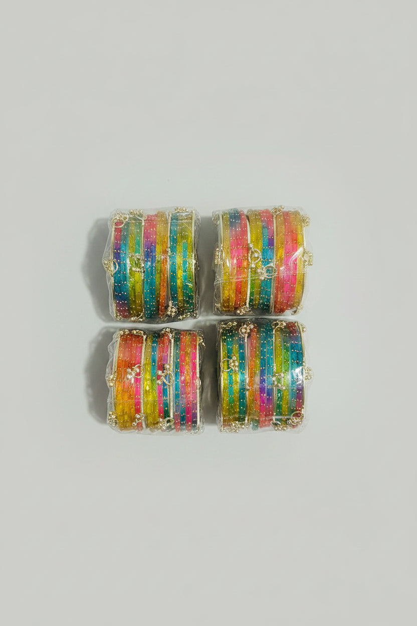 Four rolls of colorful metallic bangles with gold glitter, wrapped in clear plastic, arranged on a black polka-dot fabric background.