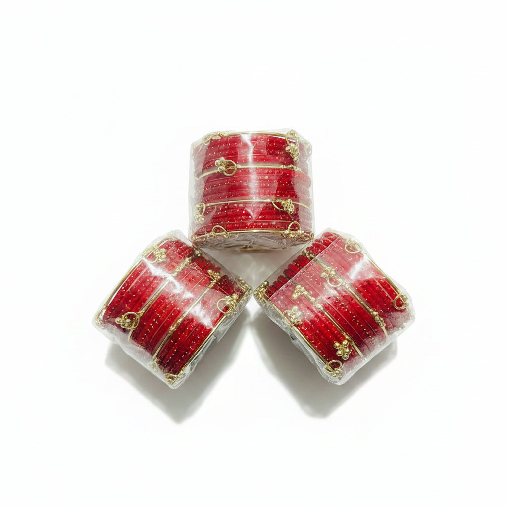 Three small stacks of red bangles wrapped in clear plastic, placed on black gift paper with gold polka dots and a woven straw-like prop in the corner.