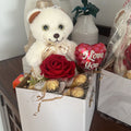 Gift box with teddy bear, roses, and 'I Love You' balloon on a wooden surface.