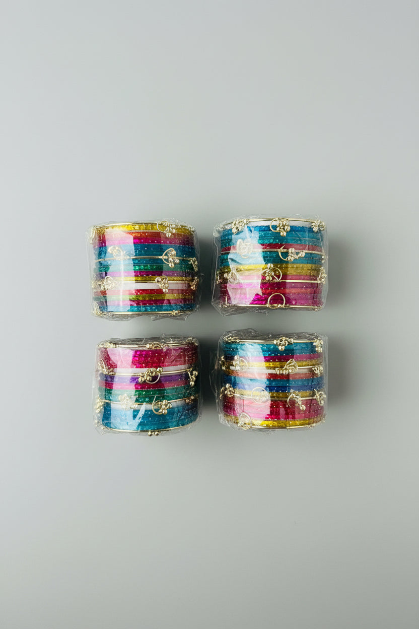 Four clear plastic-wrapped stacks of colorful bangles with gold-tone decorative elements, arranged on a woven straw surface.