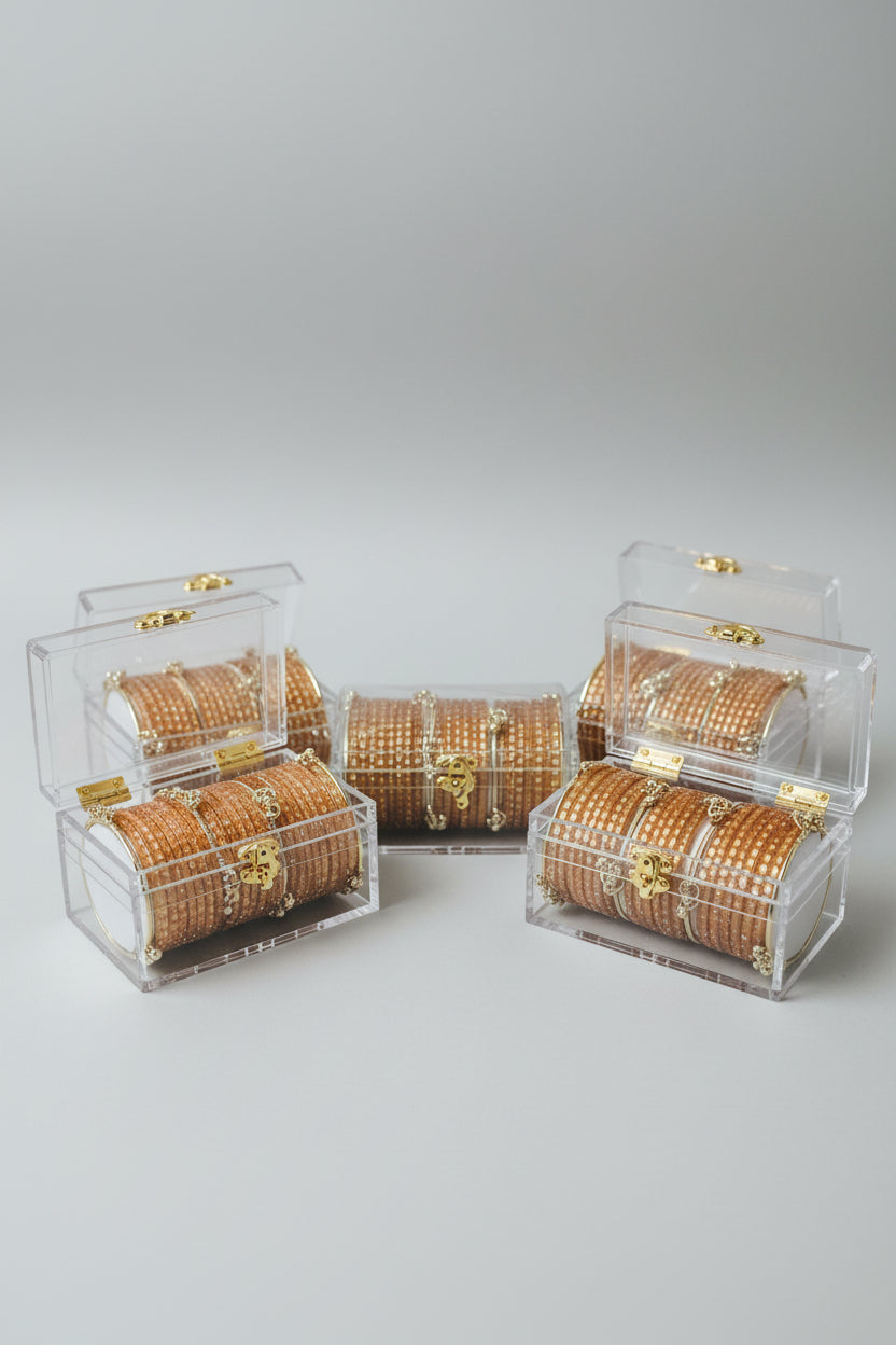 Several clear plastic-wrapped rose gold beaded bracelets with gold-toned decorative hardware are arranged on a black surface with gold polka dots.