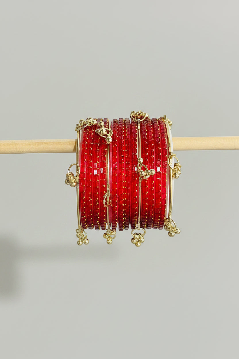 A stack of red bangles with gold foil patterns and small gold charms, displayed on a wooden stick over a black gift box with gold polka dots.