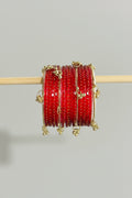 A stack of red bangles with gold foil patterns and small gold charms, displayed on a wooden stick over a black gift box with gold polka dots.